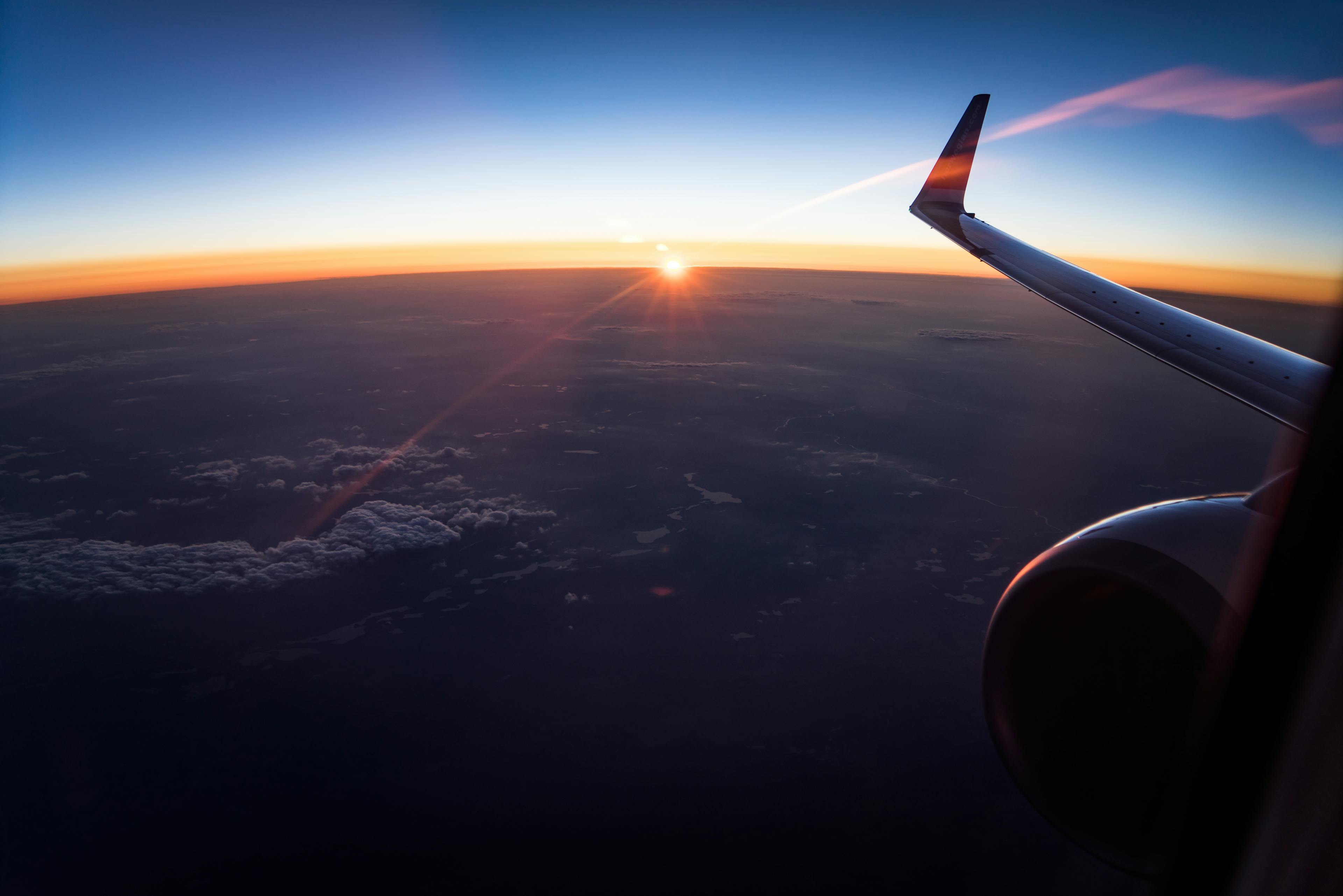 Stunning aerial view from an airplane window showing the wing and a sunset over the clouds.