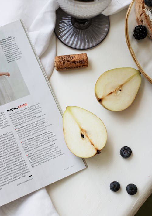 A Sliced Pear Fruit Beside the Magazine