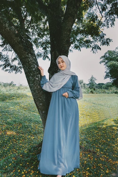 A Woman in Blue Dress with Hijab Standing Beside a Tree