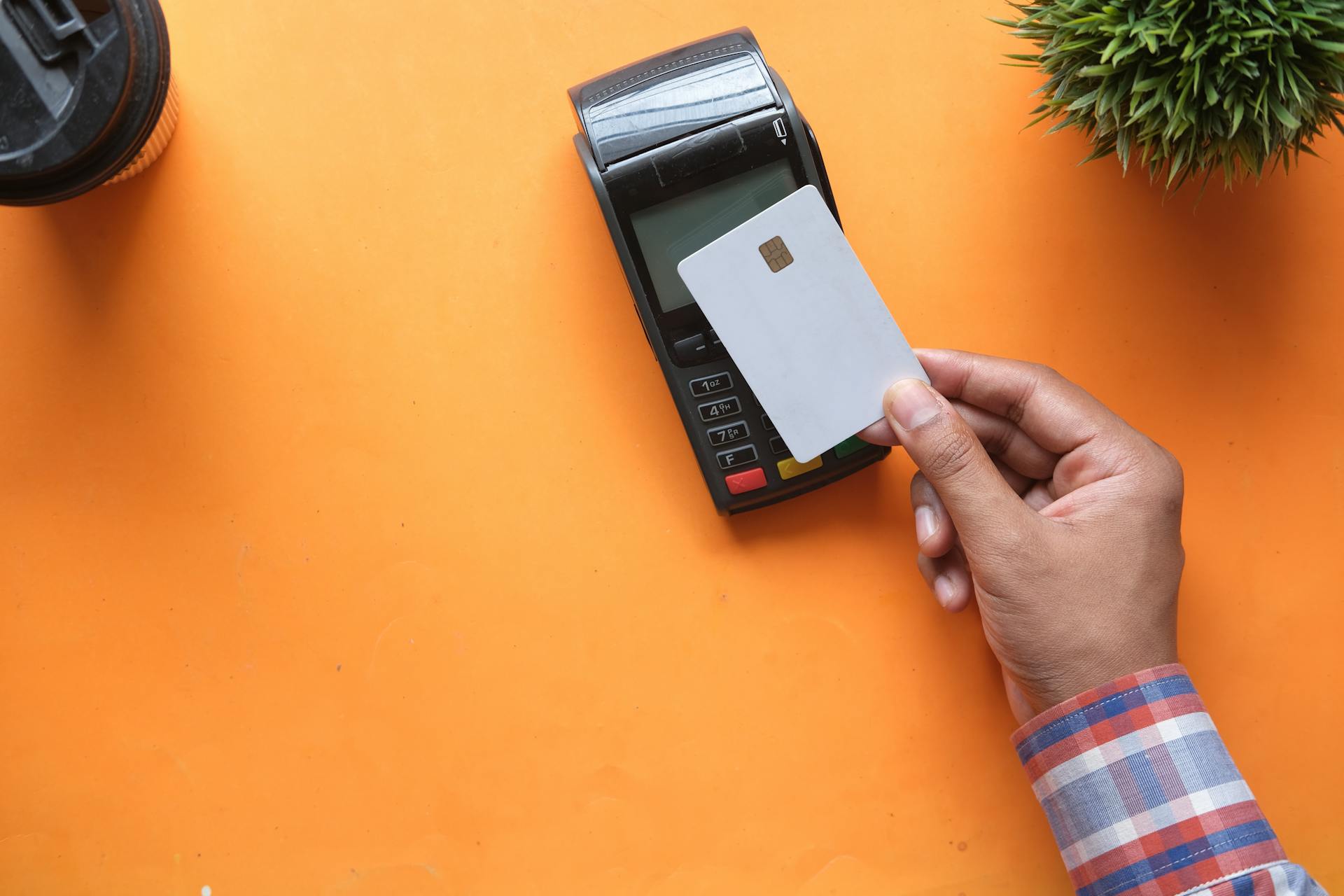 A person making a contactless payment with a credit card and card reader on a bright orange surface.