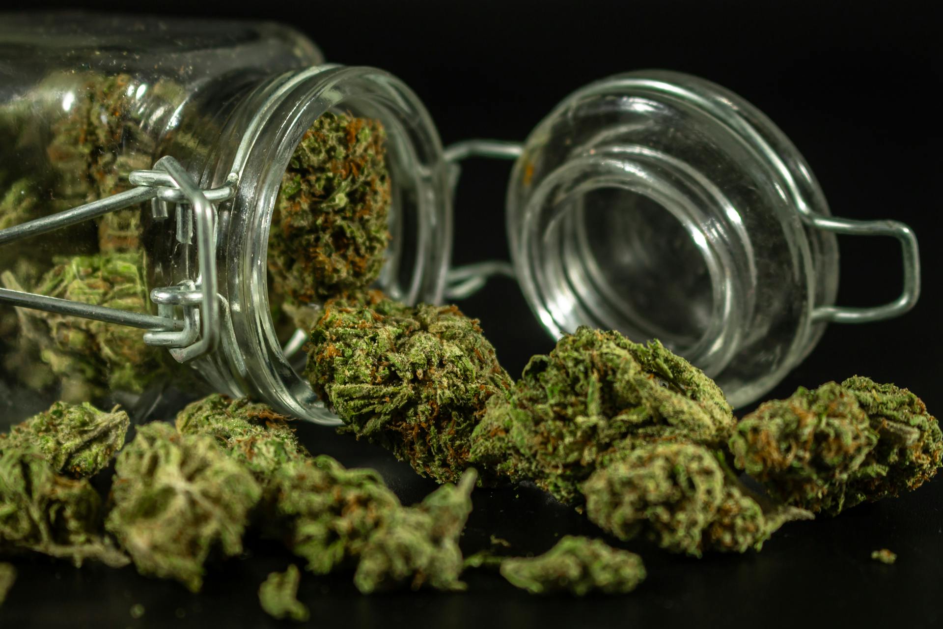 Detailed image of cannabis buds spilling out of a glass jar.