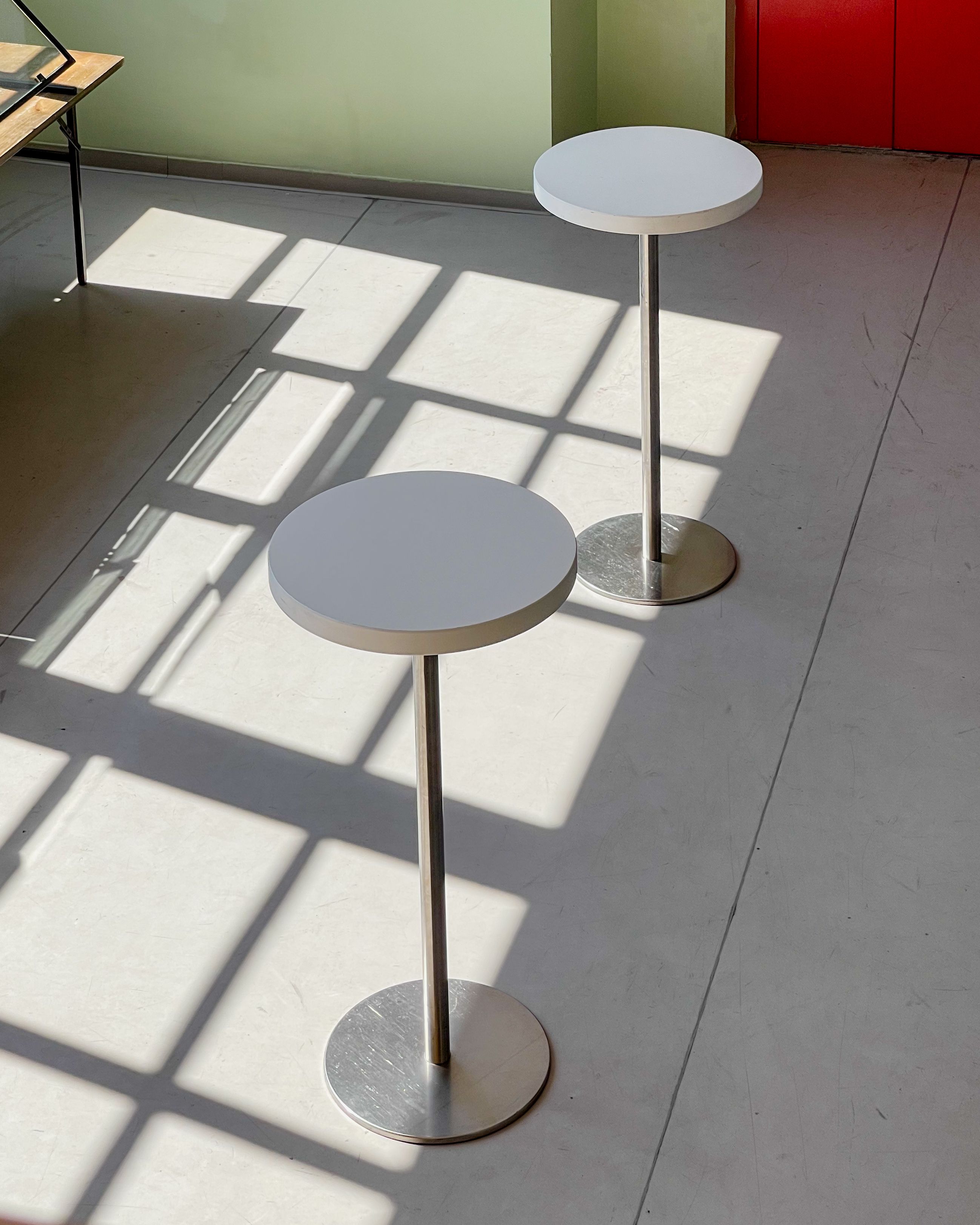 Sunlight casts geometric shadows on modern round cafe tables indoors.