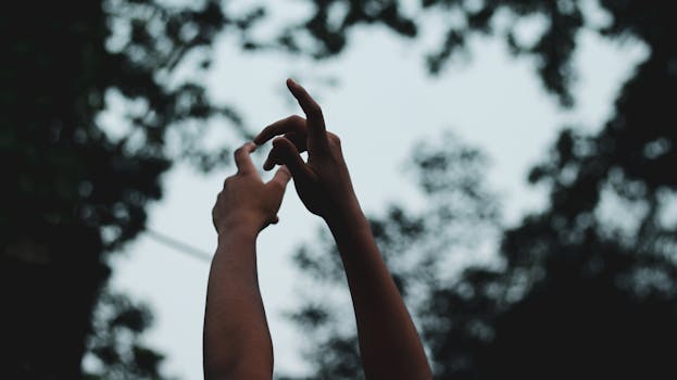 Close-up of hands reaching towards the sky outdoors against a blurred leafy background.