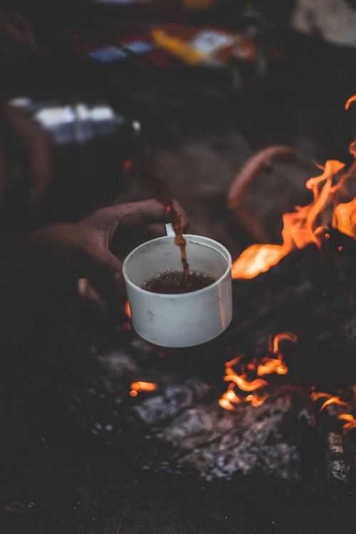 Free A rustic scene of coffee being poured over a campfire, evoking warmth and adventure. Stock Photo