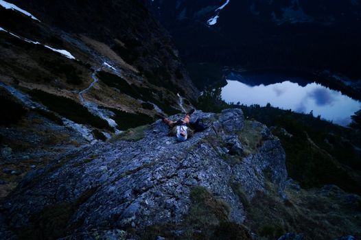 黄昏时分，一名孤独的徒步旅行者躺在岩石上，欣赏山间宁静的湖景