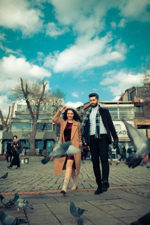 Free A stylish couple walks through a lively square in İstanbul, surrounded by pigeons. Vibrant city scene. Stock Photo