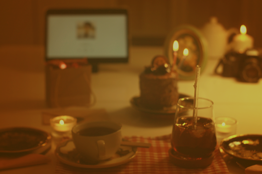 A warm, moody still life of a workspace featuring coffee, cake, and candles for a cozy ambiance.