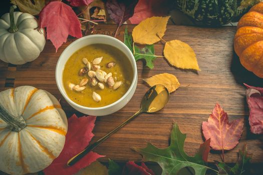 Bowl of pumpkin soup surrounded by autumn leaves and decorative pumpkins.