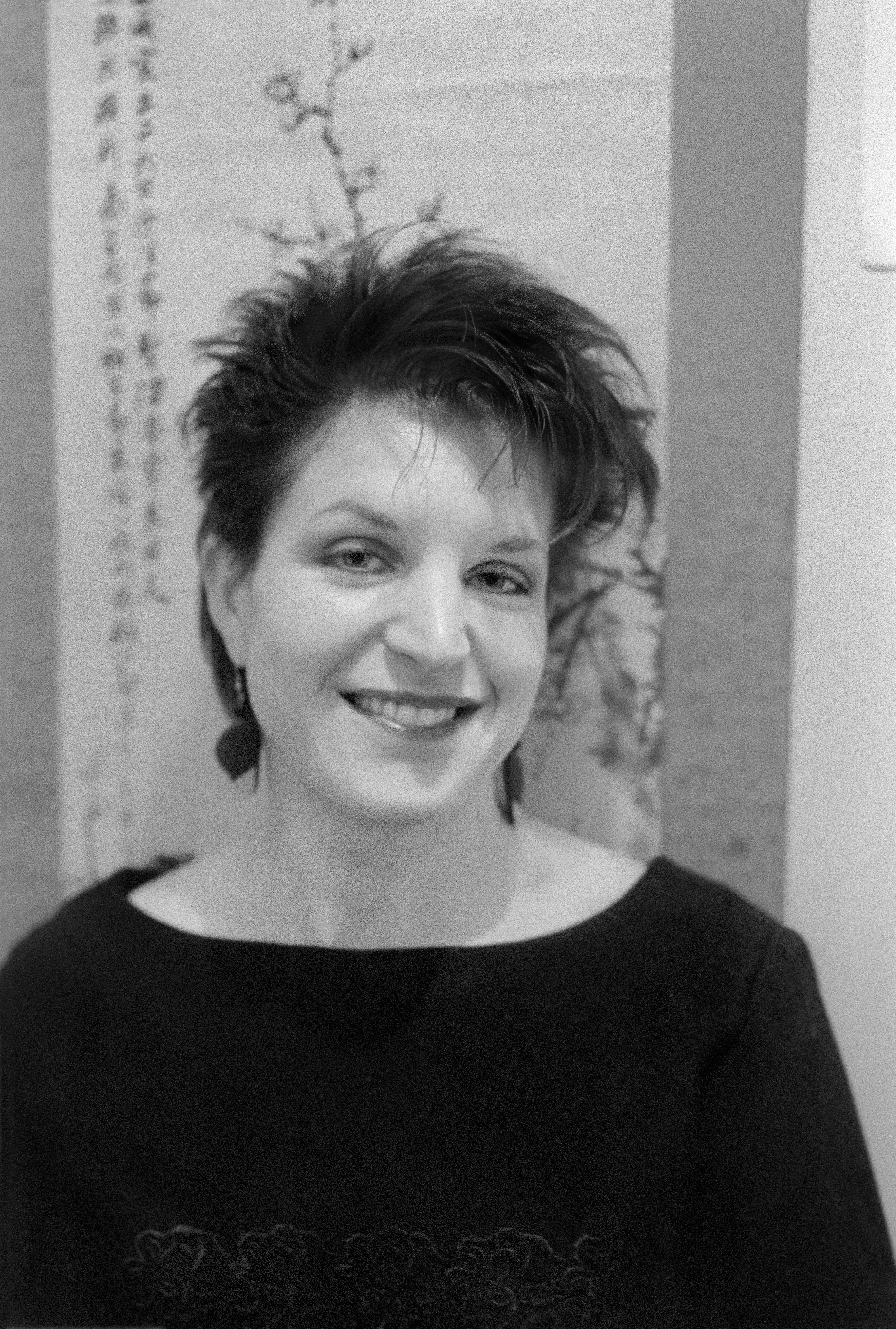 Black and white portrait featuring a smiling woman with short hair and artistic background.