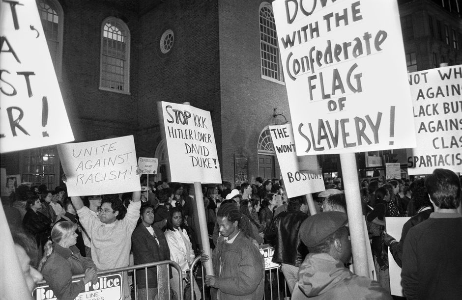 Black and white image of a diverse crowd protesting against racism, holding impactful signs.