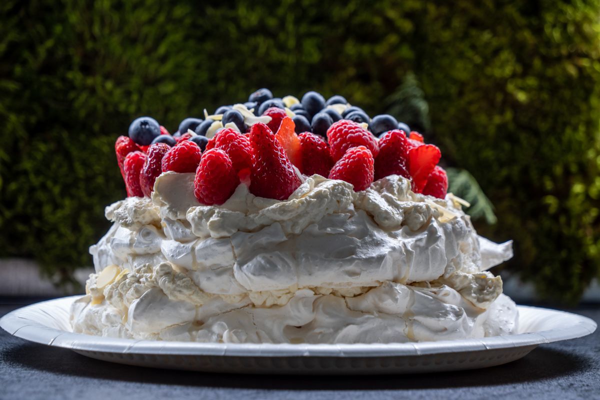 Tall layered meringue pavlova with whipped cream, heaped raspberries and blueberries on a plate