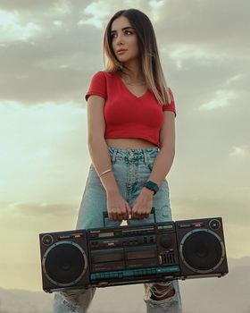 Stylish young woman in ripped jeans holds a boombox outdoors in Tehran.