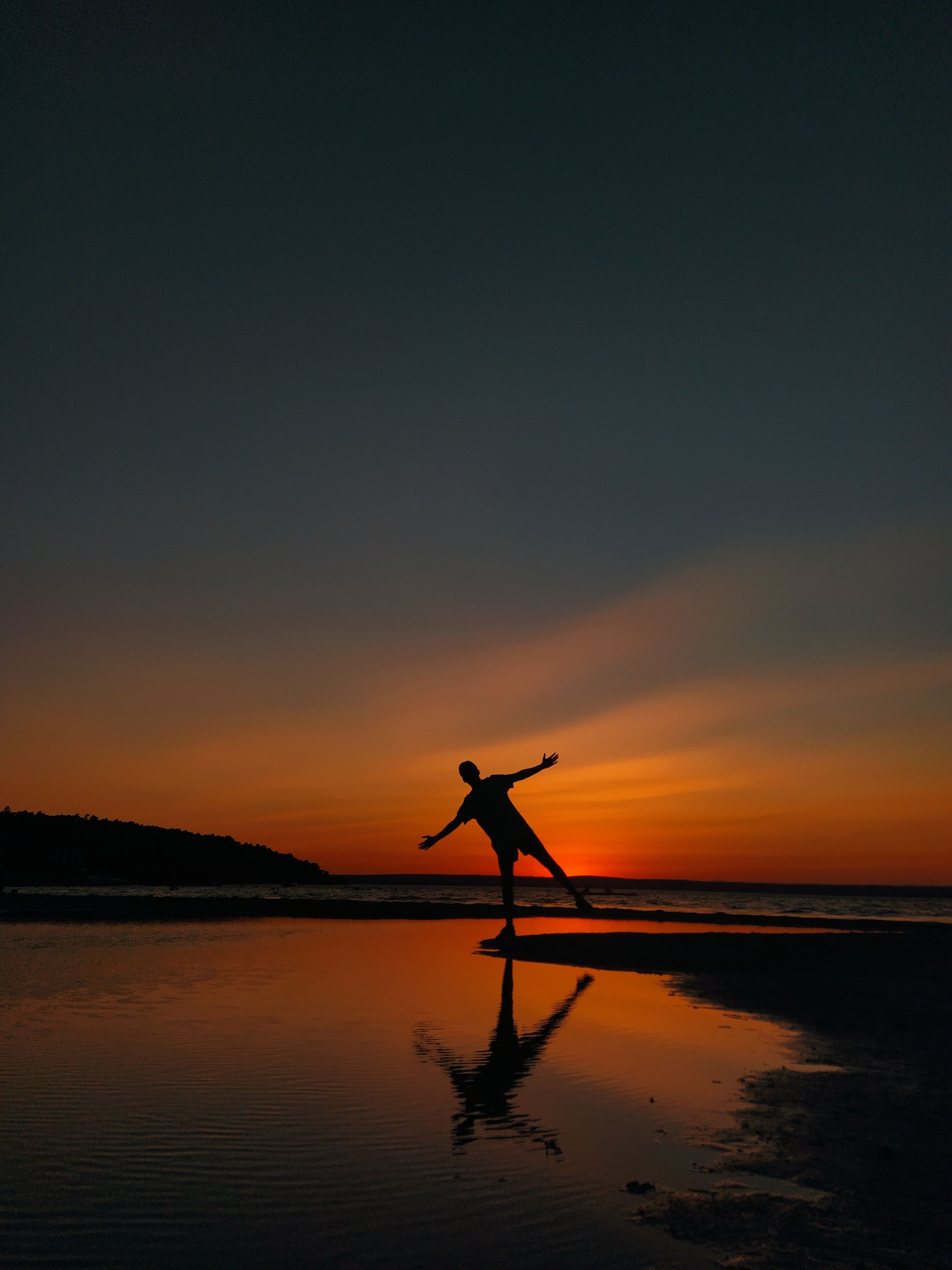 A person silhouetted against a vivid sunset over a beach in Akbük, Turkey, creating a tranquil scene.