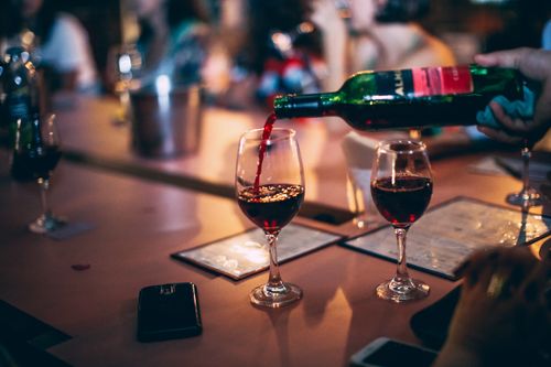 Free Red wine being poured into glasses at a vibrant bar scene, creating a warm atmosphere. Stock Photo