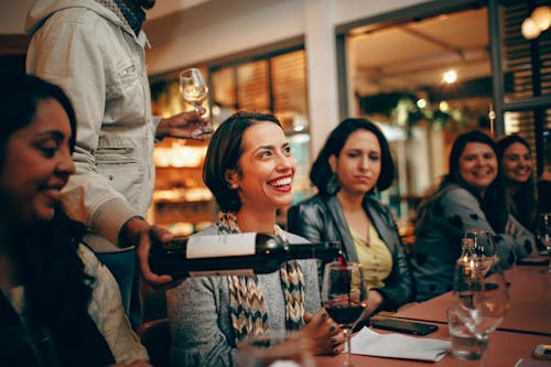 Happy Woman beside Person pouring Wine on a Glass