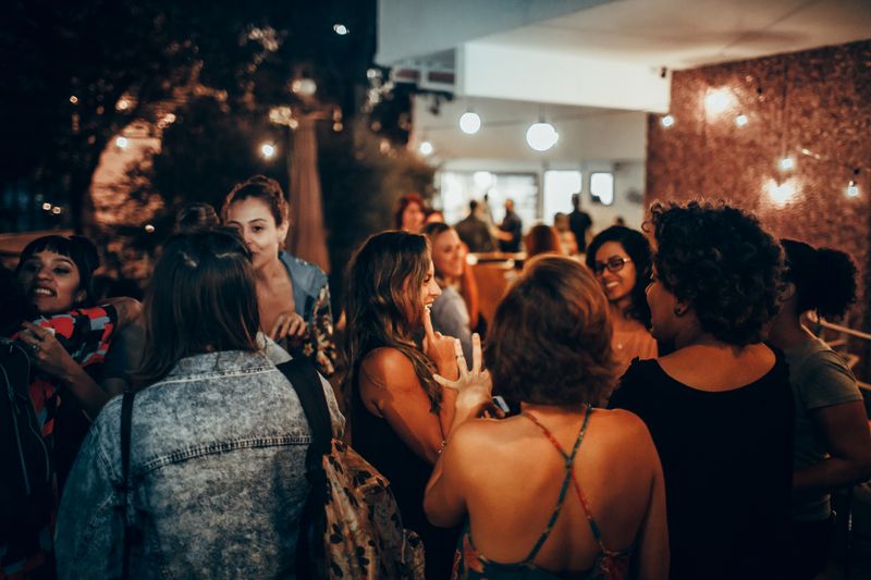Evening gathering of people talking outdoors under warm lights — photo by Helena Lopes on Pexels