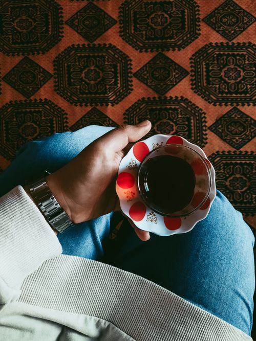 Free A cozy setting with a person holding a tea cup over a patterned carpet, capturing warmth. Stock Photo