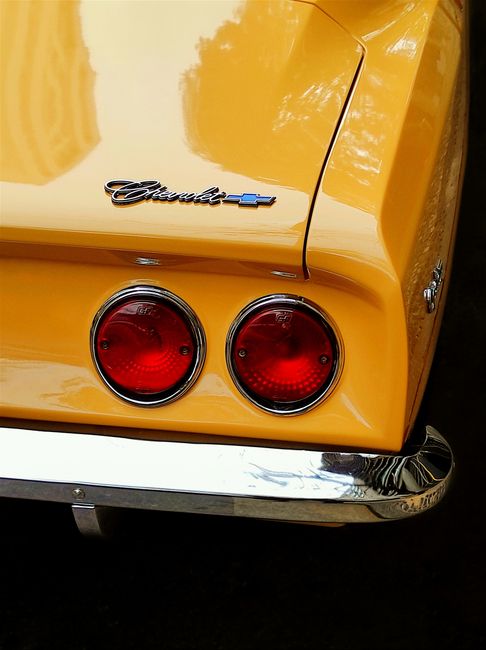 Close-up of a vintage yellow car's tail lights, showcasing classic design and glossy finish.