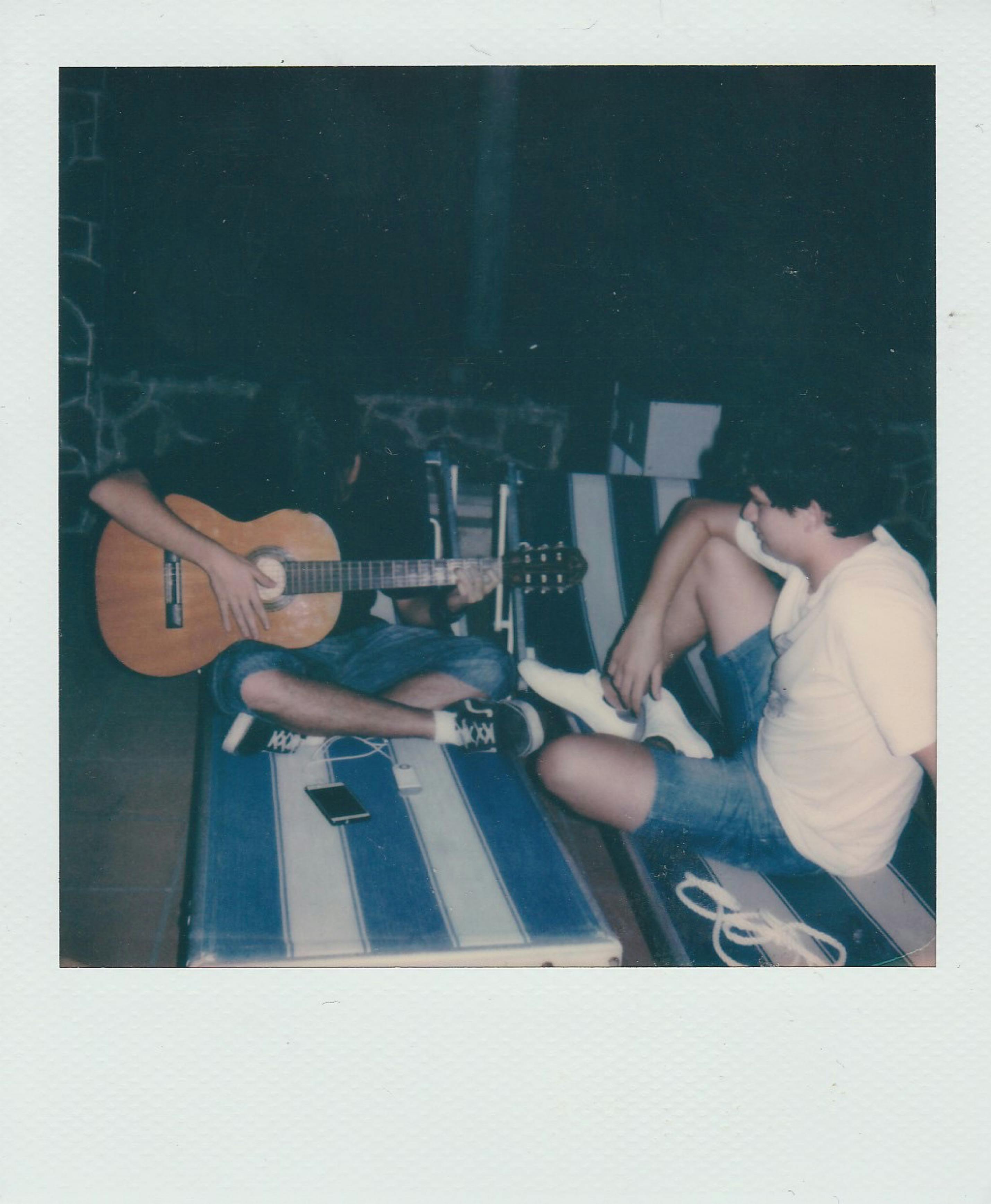Two friends relax on beach chairs, one playing guitar, creating a musical vibe.
