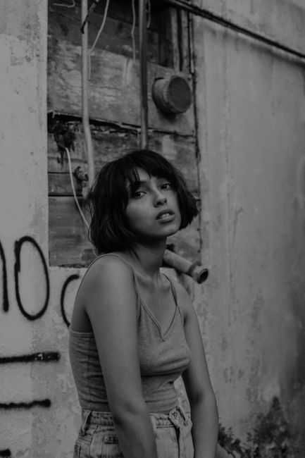 Black and white portrait of a young woman posing outdoors against an urban backdrop.