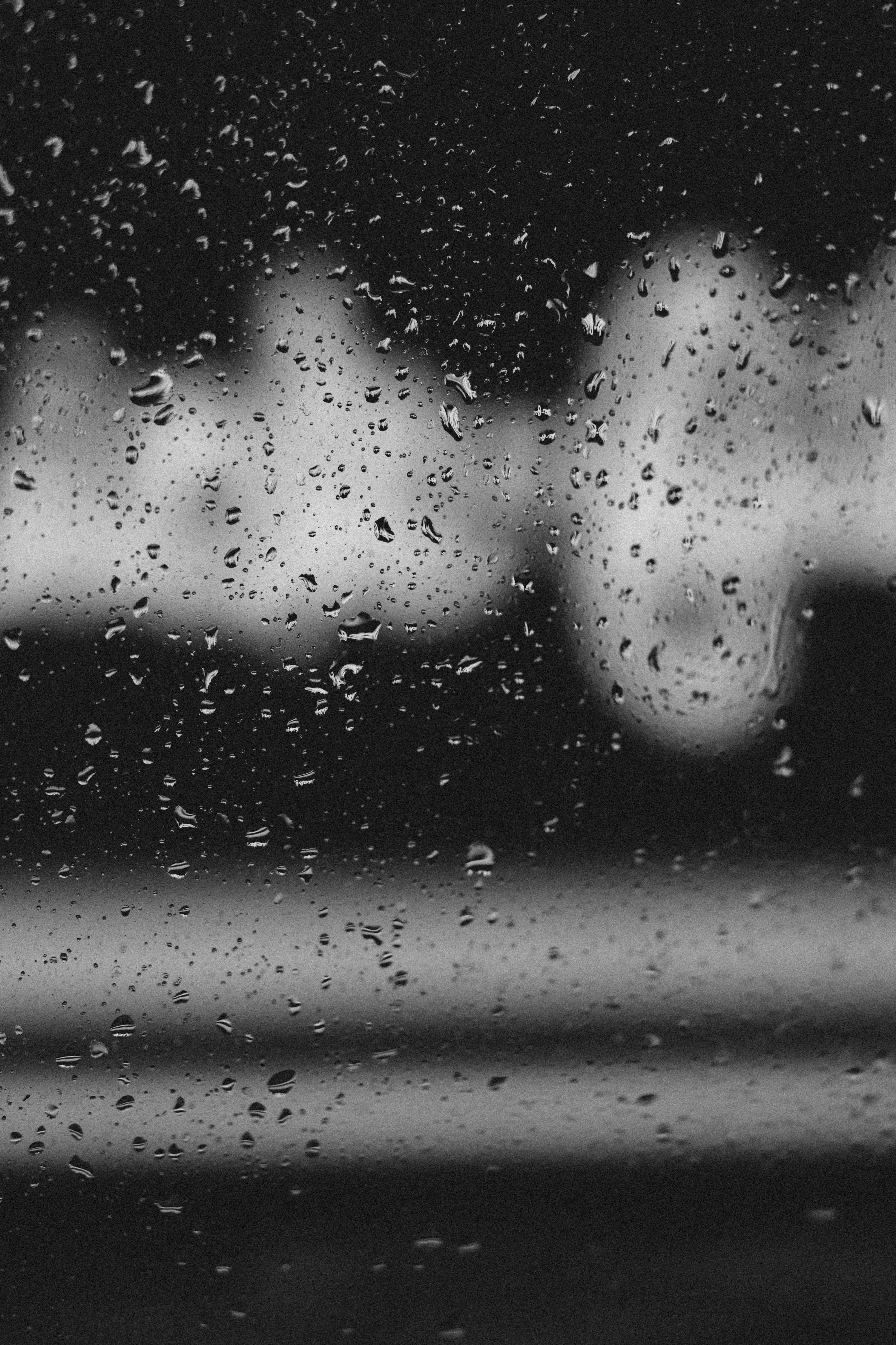 Monochrome photo capturing raindrops on a window with blurry cityscape in the background.