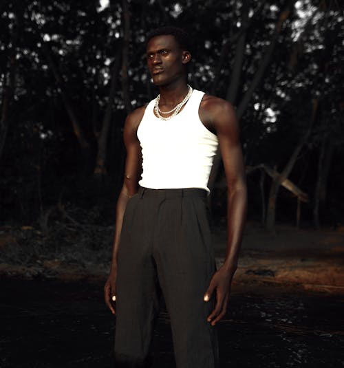 Man in White Tank Top and Brown Pants Standing on Dirt Road