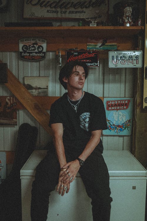 A Man in Black Shirt Sitting on the Freezer