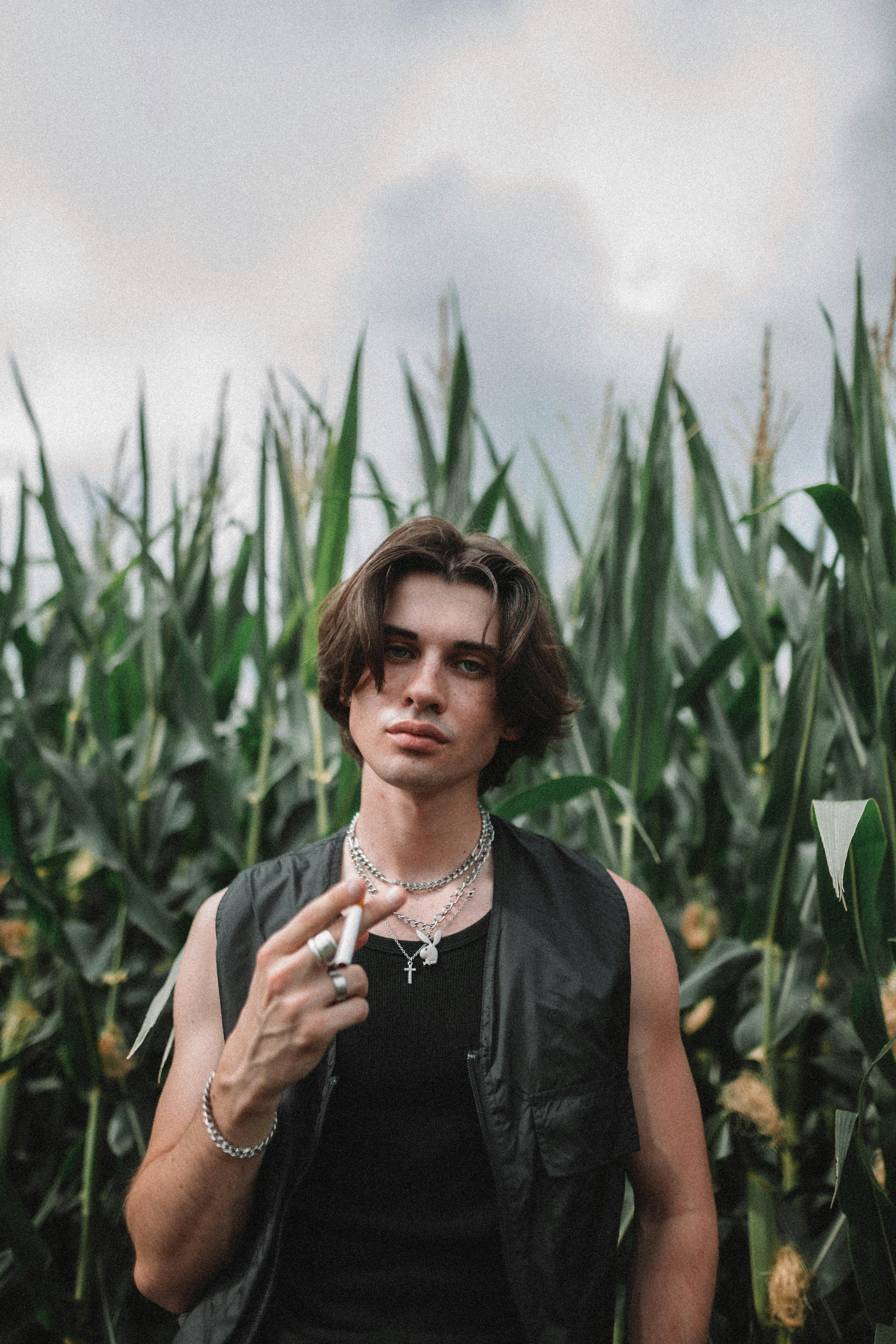 Young man with modern fashion poses confidently in a lush green cornfield.