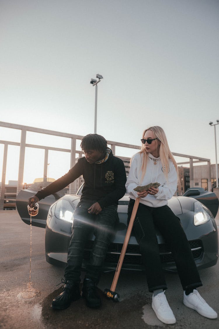 Couple With Drink Sitting On Car Hood