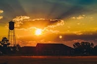 戏剧性的日落与水塔和农舍的剪影，共同构成了一幅引人注目的农村景象