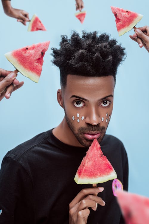 Man in Black Crew Neck Shirt holding Sliced Watermelon on Stick 