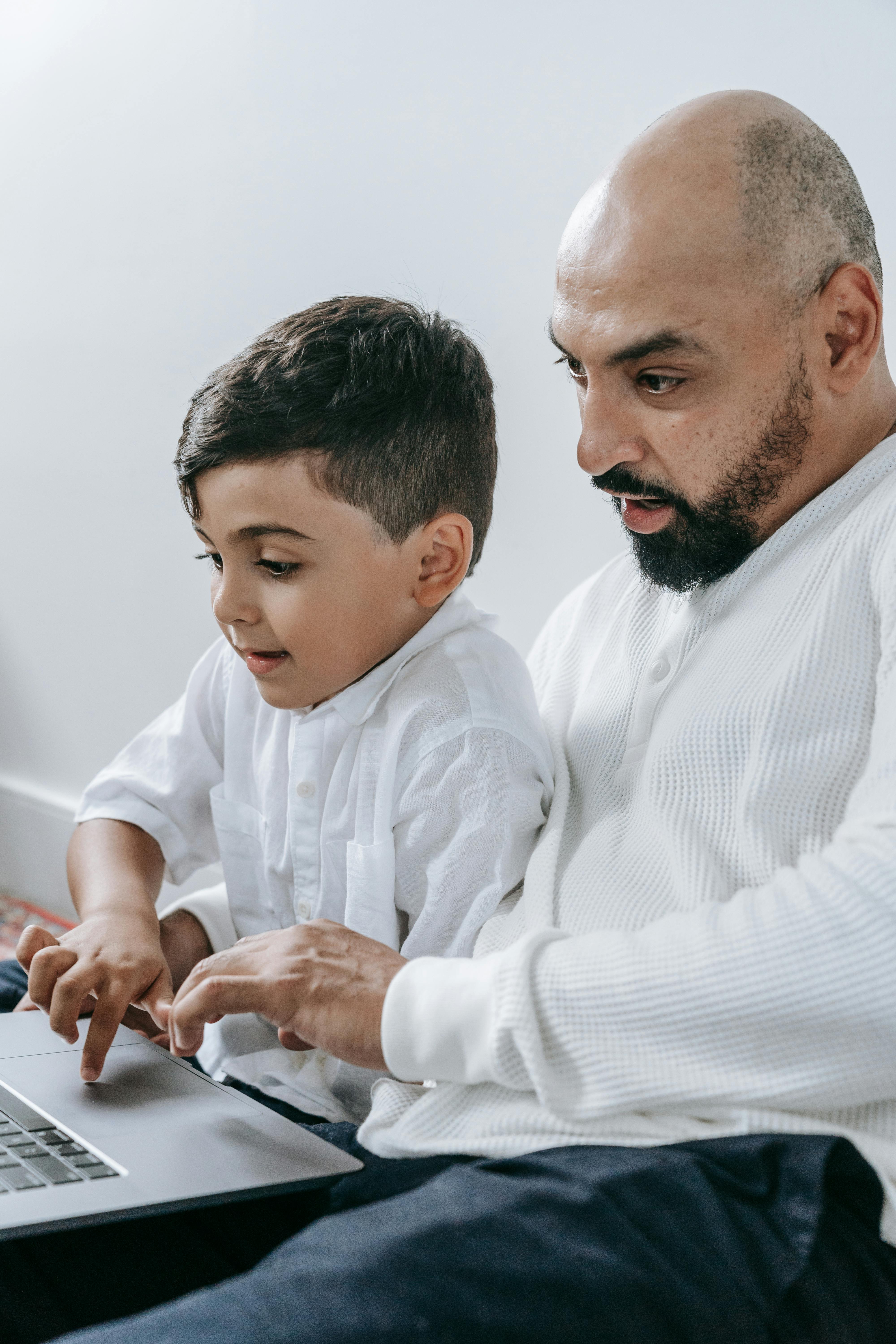 Father and son sitting together using a laptop, sharing quality family time indoors.