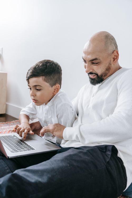 Free A father and son sharing a bonding moment while using a laptop indoors. Stock Photo