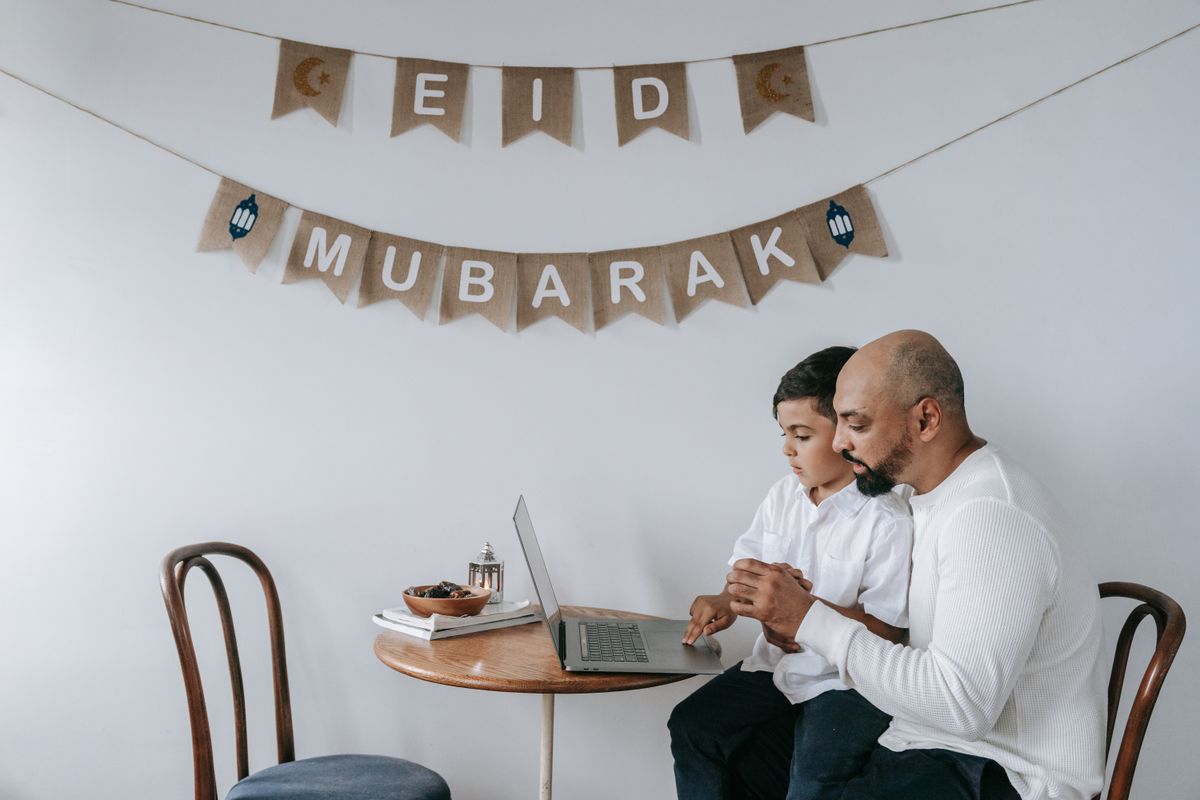 توقيت الرسائل الآلية في رمضان أب وابنه على طاولة مزيّنة بعبارة عيد مبارك
