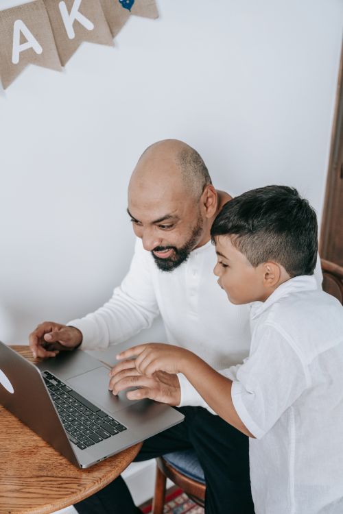 Free A joyful father and son share a bonding moment while using a laptop together. Stock Photo