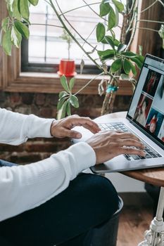 Close-up of hands typing on a laptop by a window with indoor plants.