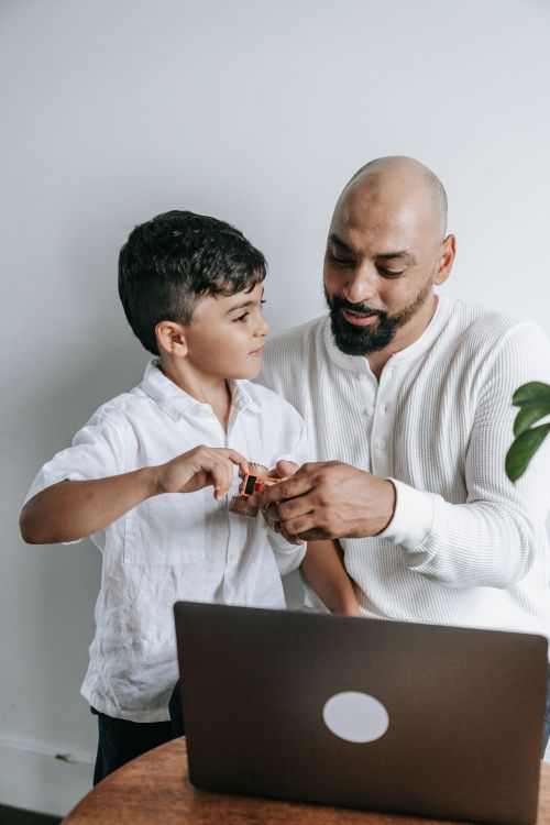 Free Father and son enjoying technology time together at home using a laptop. Stock Photo