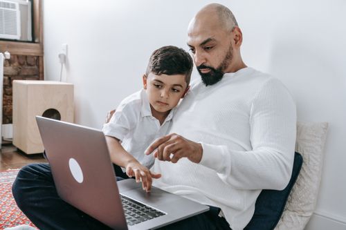 Free A father and son bonding at home while looking at a laptop screen together. Stock Photo