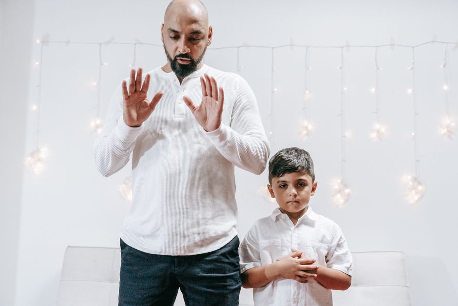 Pai e filho em camisetas brancas orando juntos em casa, com iluminação suave