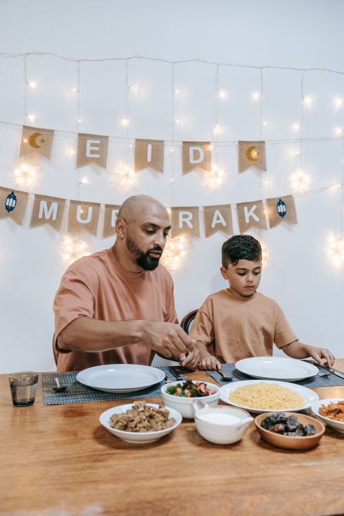 Free Father and son share a meal during Eid celebration, with festive decorations. Stock Photo