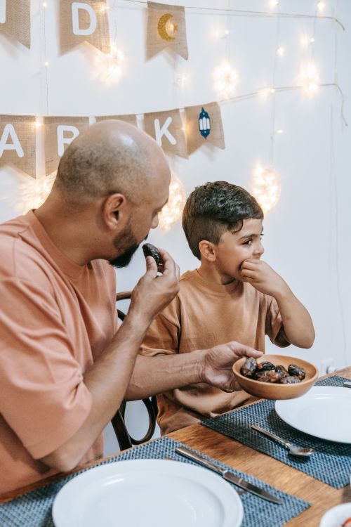 Free Father and son enjoying a festive Eid meal together indoors with dates. Stock Photo