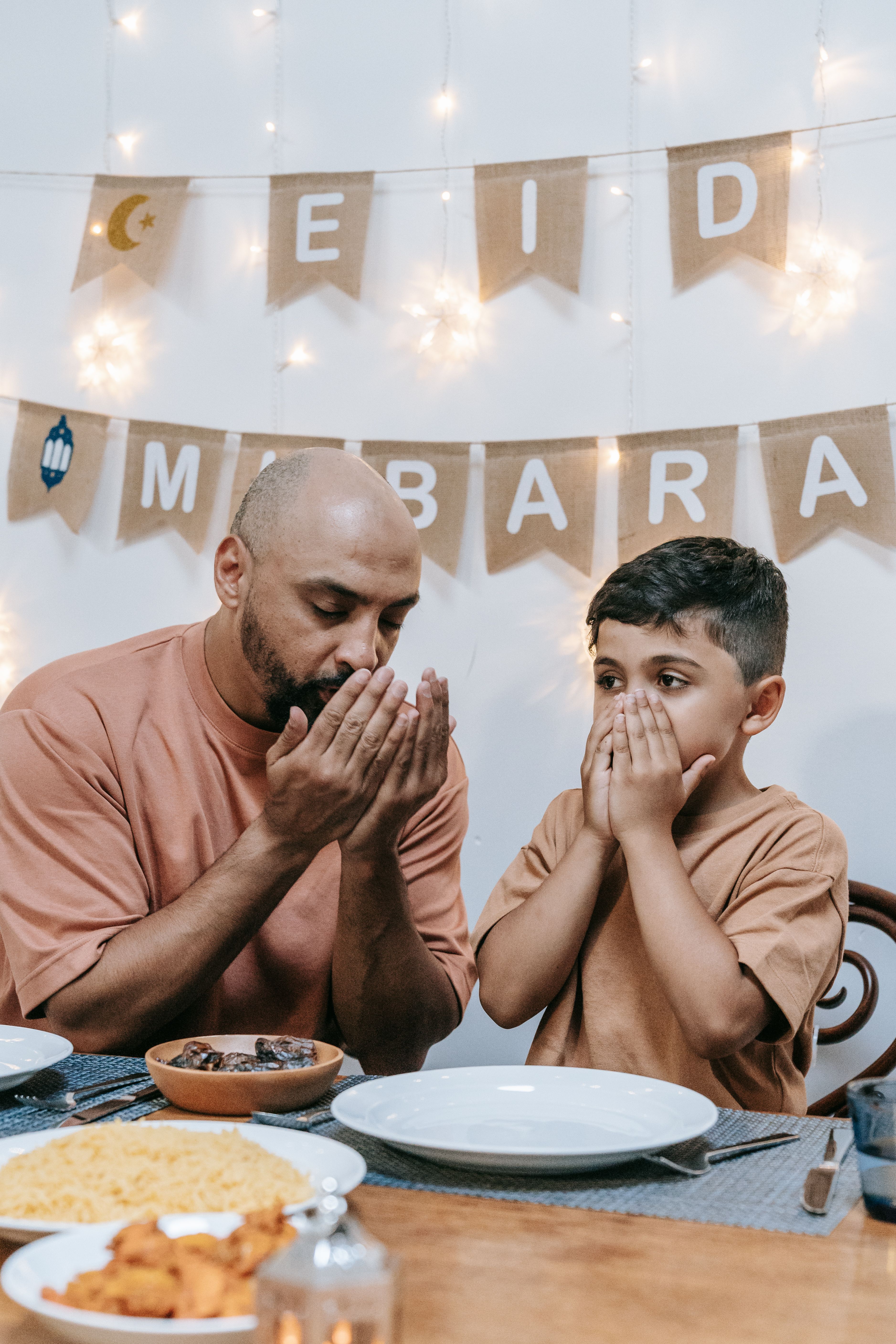 Father and son praying before a festive Eid meal, featuring traditional dishes.