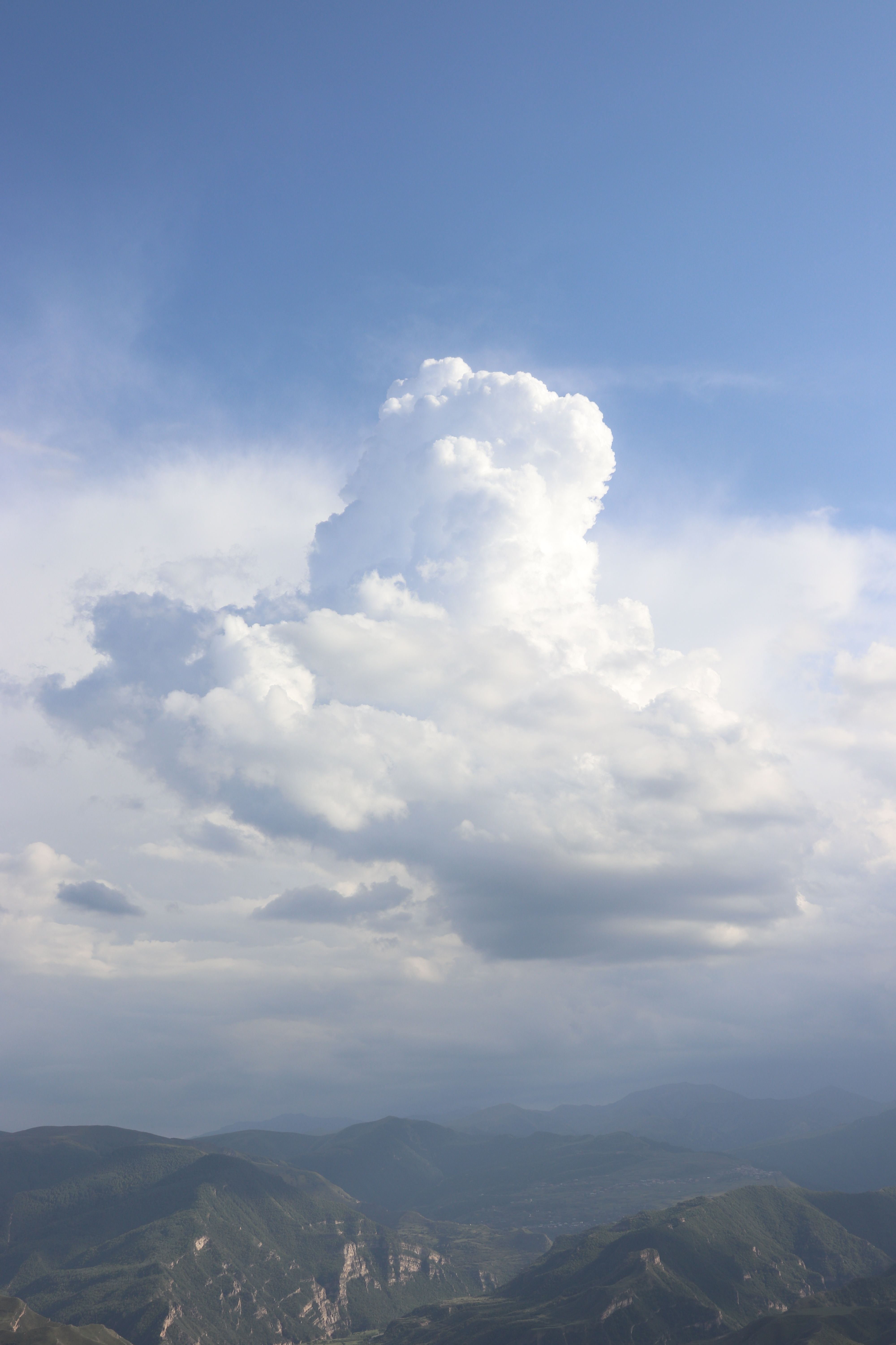 Dramatic cloud formation towers over scenic mountains, reflecting nature's grandeur.