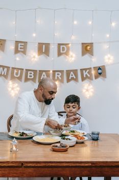 Father and son enjoying a festive Eid meal together indoors, creating cherished family moments.