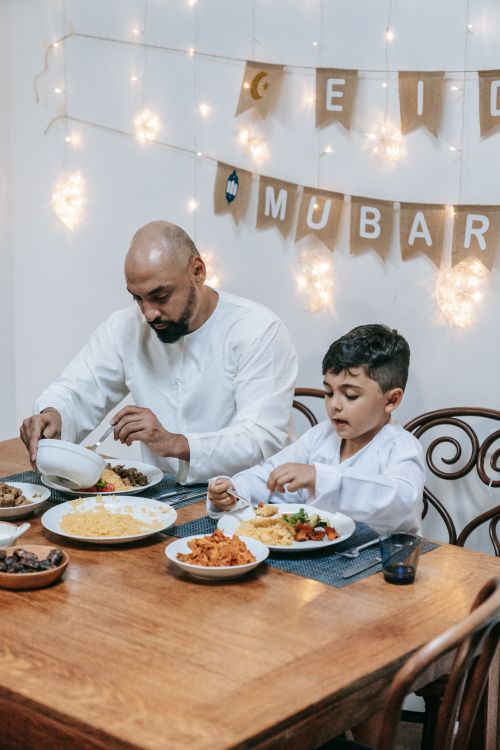 Free Father and son enjoying an Eid meal together indoors. Eid Mubarak decoration adds festive ambiance. Stock Photo