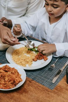 A young child eating a plate of noodles and fried chicken with adult assistance.