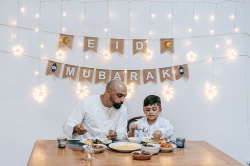 Free A father and son enjoy a meal together during an Eid celebration with festive decor. Stock Photo