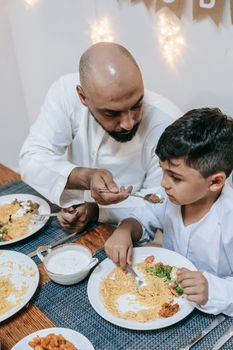 A father lovingly feeds his son at a family dinner, celebrating a cultural or religious festival.