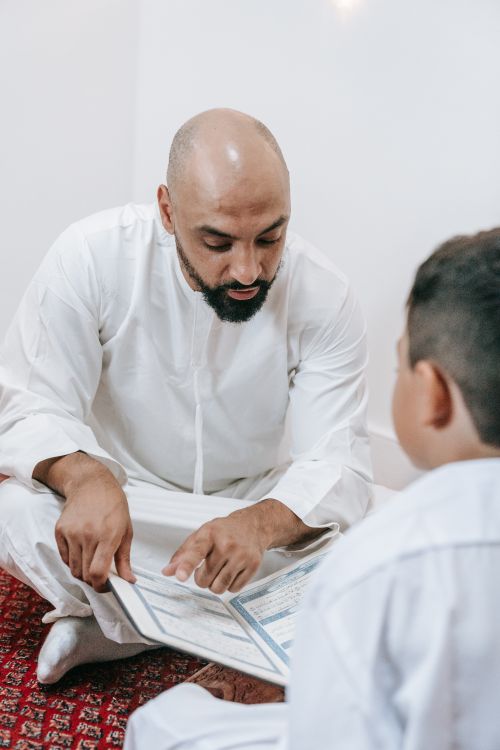 Free A father and son in traditional attire, reading religious texts together in a peaceful setting. Stock Photo