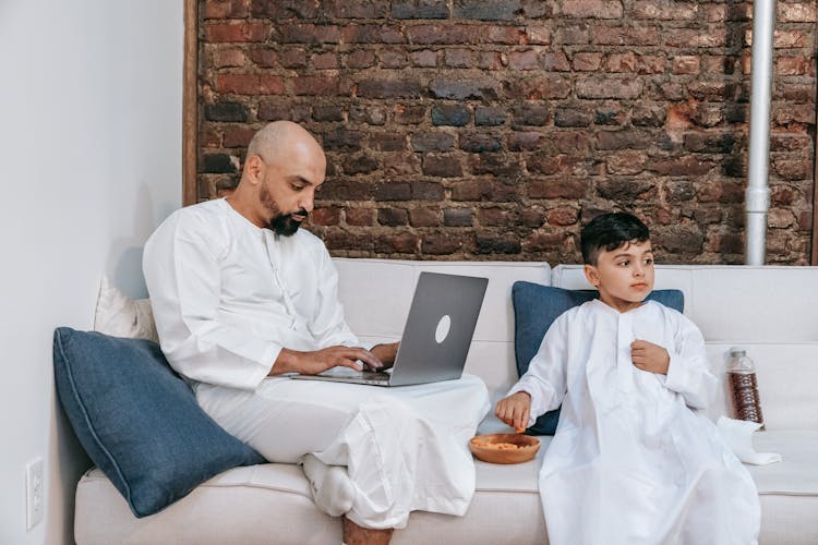 Father And Son In Traditional Clothes Sitting On Sofa